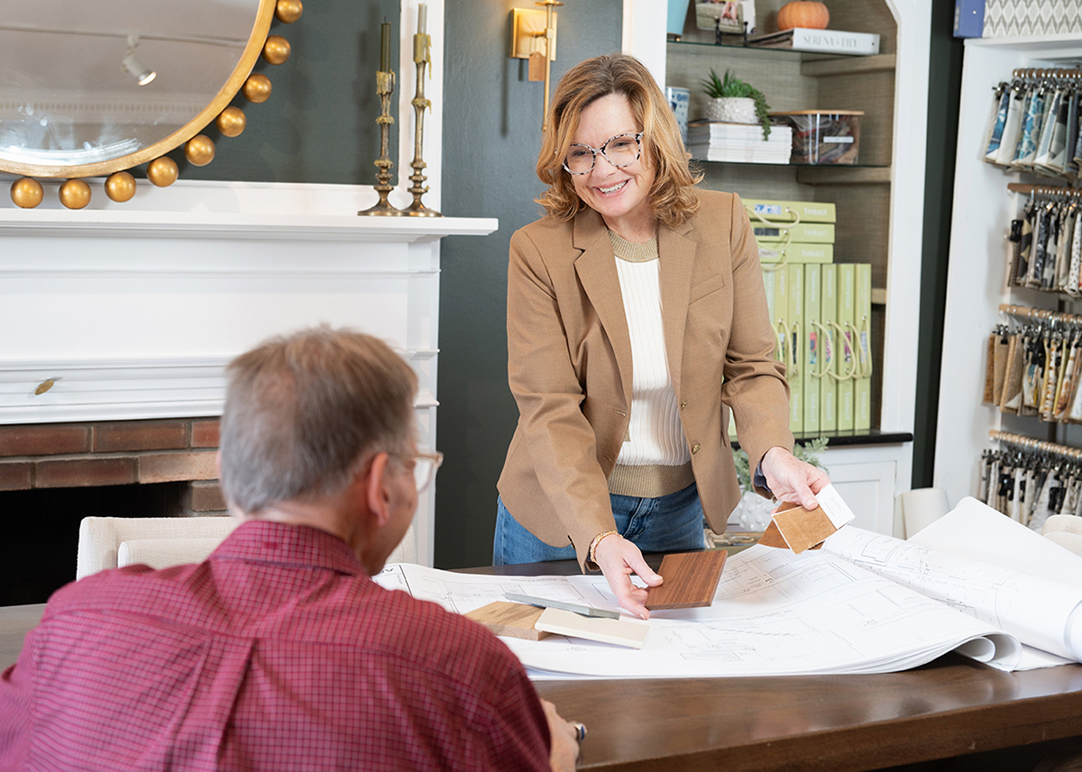 Colleen Cusick, an interior designer at McQ Interiors, in a brown blazer showing a client a hardwood flooring sample.