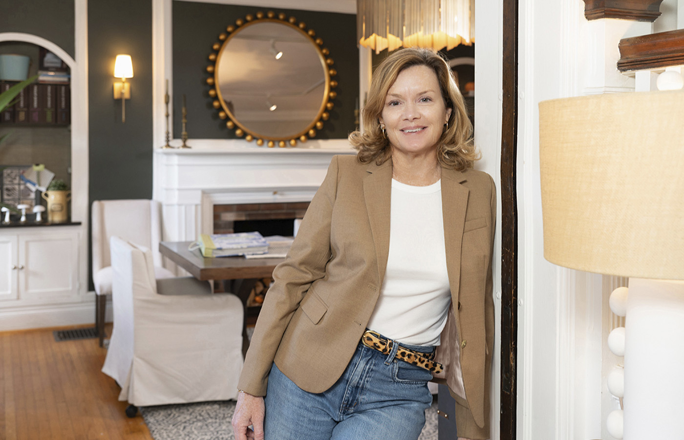 McQ Interiors owner, Colleen Cusick, in a brown blazer with a living room and work table blurred behind her.